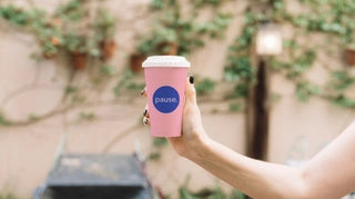 Pink custom coffee cup held in hand in an outdoor courtyard setting